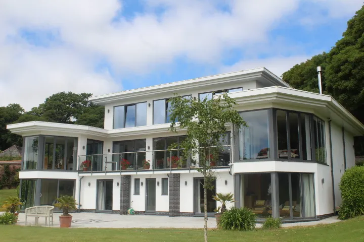 A large contemporary house with white render, balconies and a curved glazed corner, seen across its lawn.