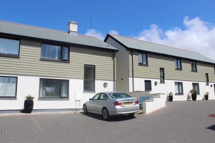 A row of newly built houses at Copperhouse Mews, Hayle, with cream weatherboard cladding, slate roofs and a block-paved parking court.
