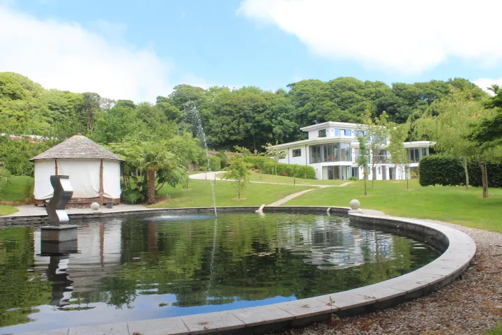 A contemporary white-rendered house seen from across a lake, with trees around the water.