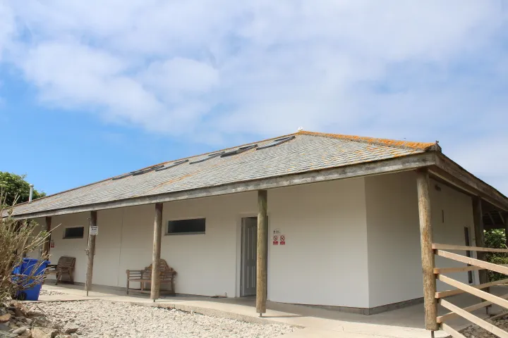 A new single-storey amenity building with a slate roof and a covered veranda on rough timber posts.