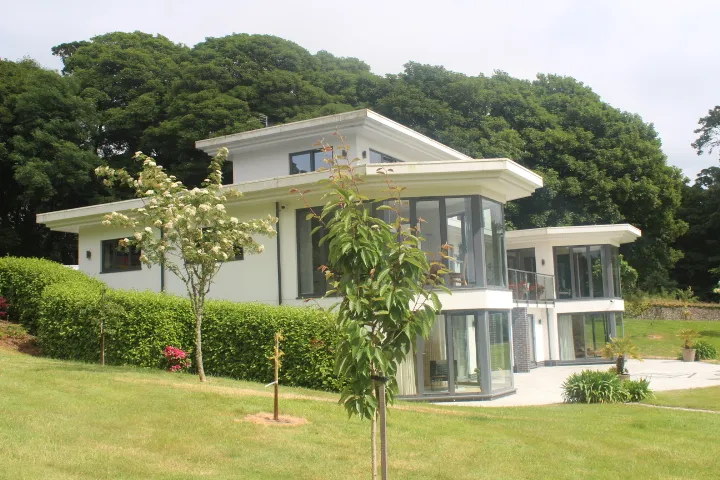 The side elevation of a contemporary white-rendered house, seen from the lawn.
