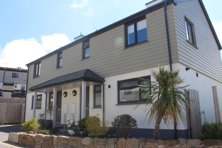 A corner house at Copperhouse Mews, Hayle, with weatherboard cladding, a porch and established planting behind a granite wall.
