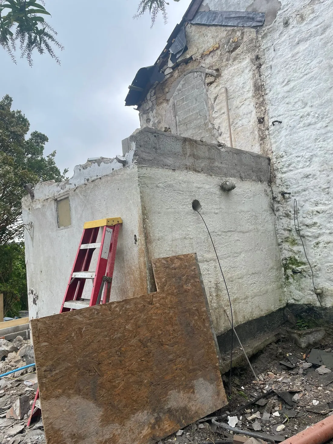 A rear outbuilding part demolished against the whitewashed granite wall of an old cottage.