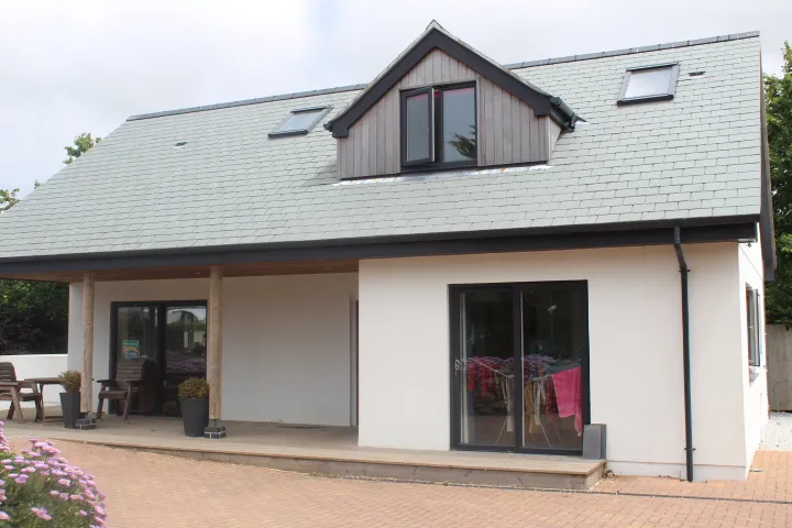 A completed house with a slate roof, timber-clad dormer, oak porch posts and block-paved drive.