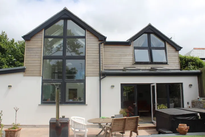 The rear of a house with two cedar-clad gables, full-height glazing and a paved terrace.