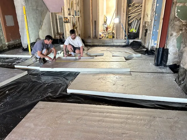Two of the team kneeling to lay floor insulation boards over a damp-proof membrane in a stripped-out interior.