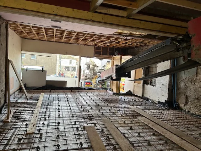 Steel beams installed above a ground floor with reinforcing mesh laid out on chairs across a new slab, open to the street at the far end.