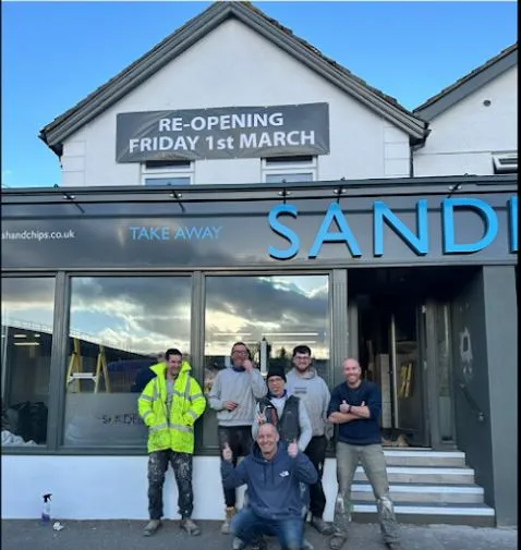 Seven of the A Nevitt Construction team standing outside a shop they have just fitted out, under a banner announcing its re-opening.