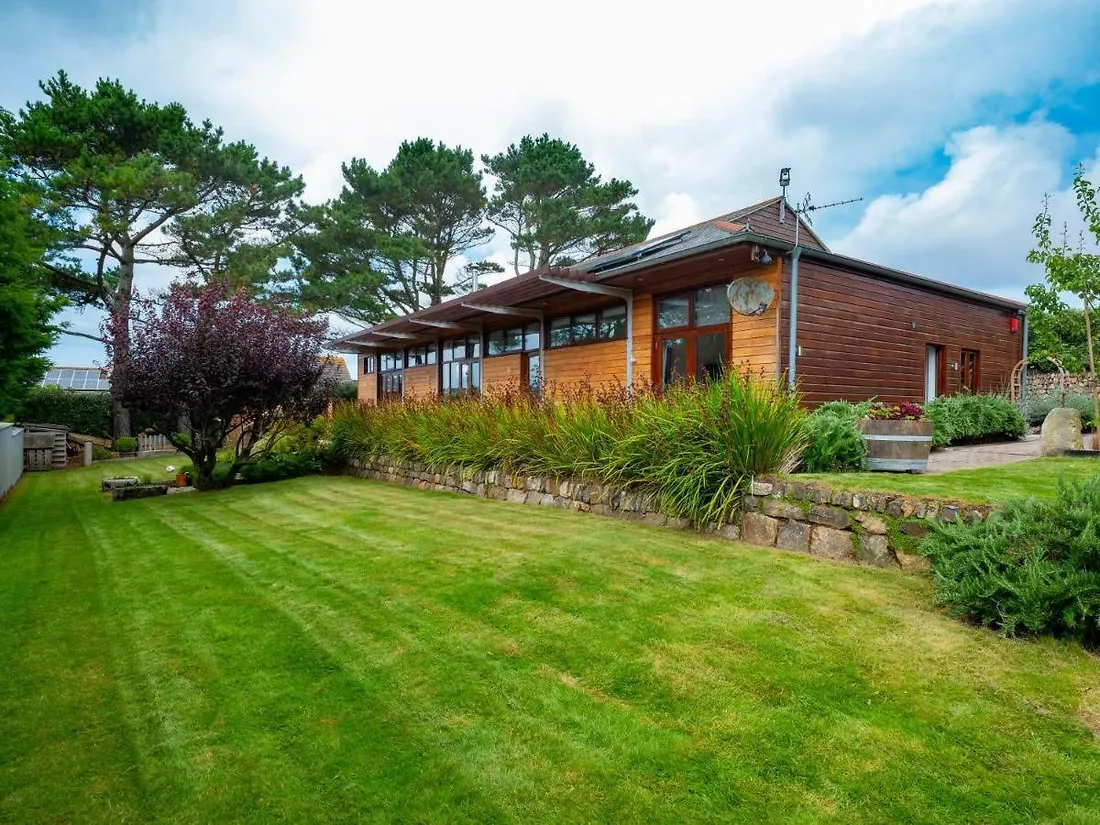 A long timber-clad single-storey building with deep eaves, above a stone retaining wall and a striped lawn.